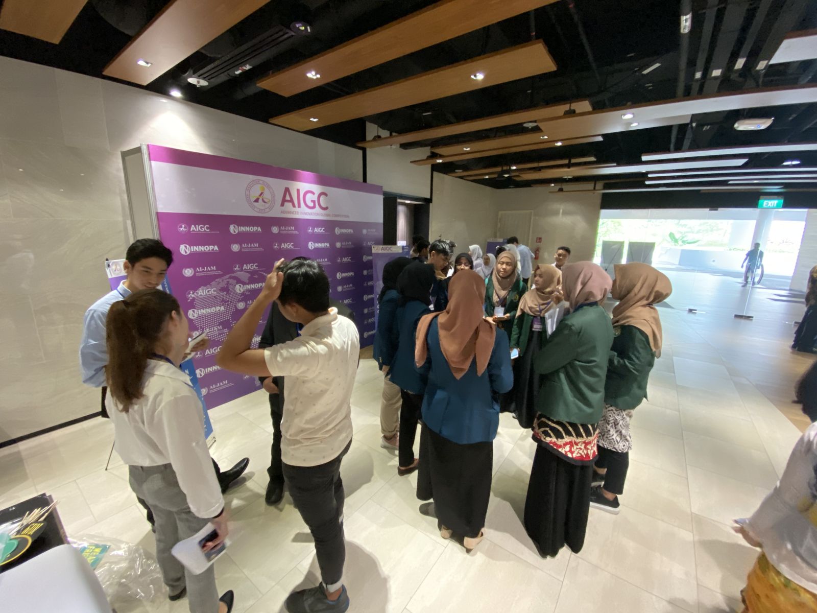 Students and organizers talking in front of the purple AIGC backdrop at the Singapore venue