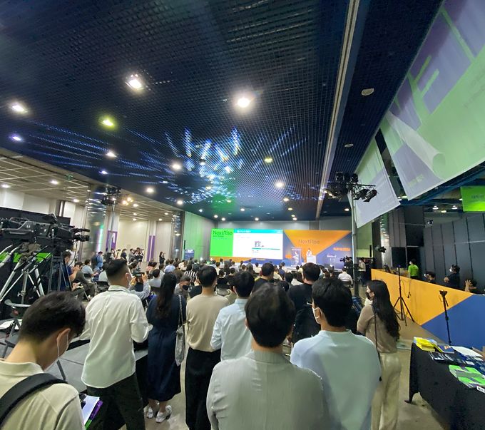 Crowd watching a keynote in a large conference hall with stage screens