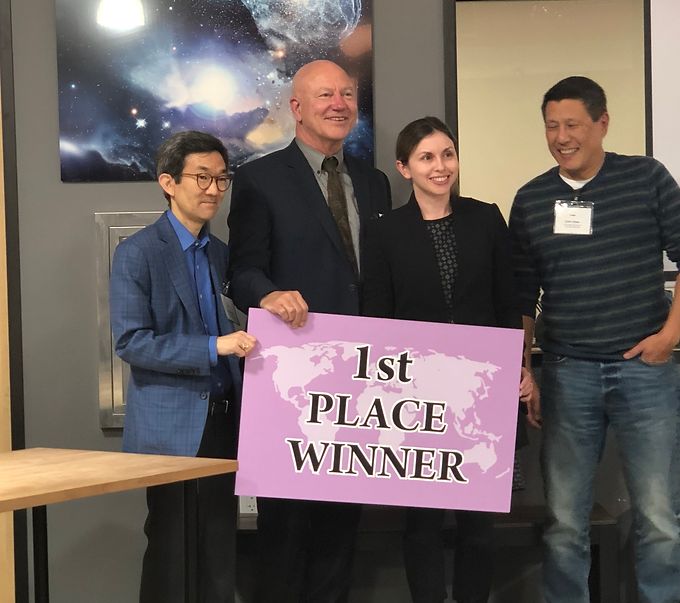 Four people holding a purple sign reading 1st Place Winner