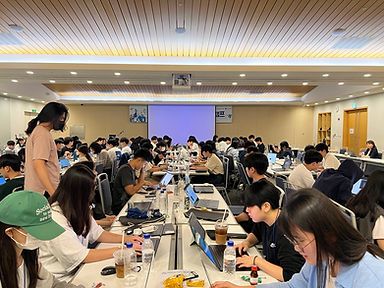 Rows of students working on laptops in a large hall during a hackathon