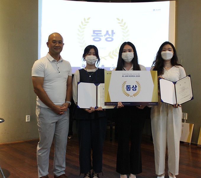 Three students holding certificates and an award board next to an organizer